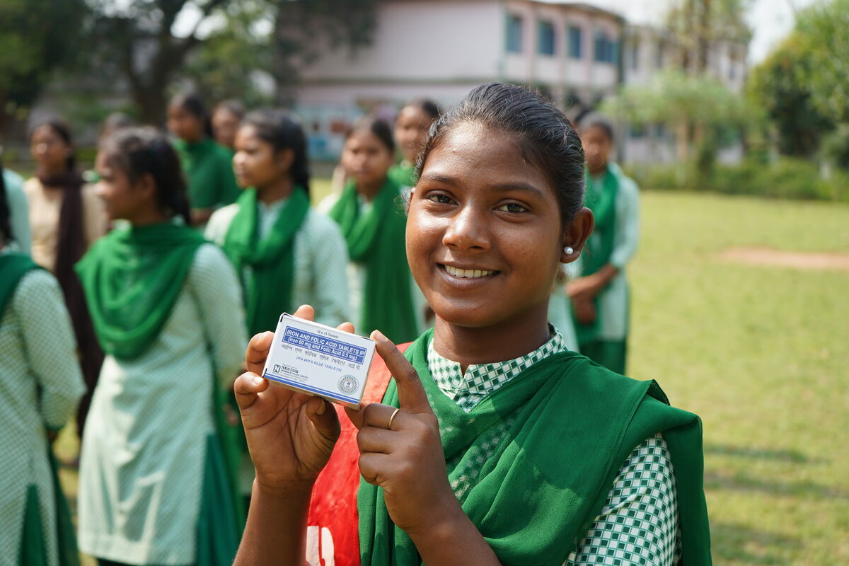 A female student in uniform holding a vitamin supplements pack