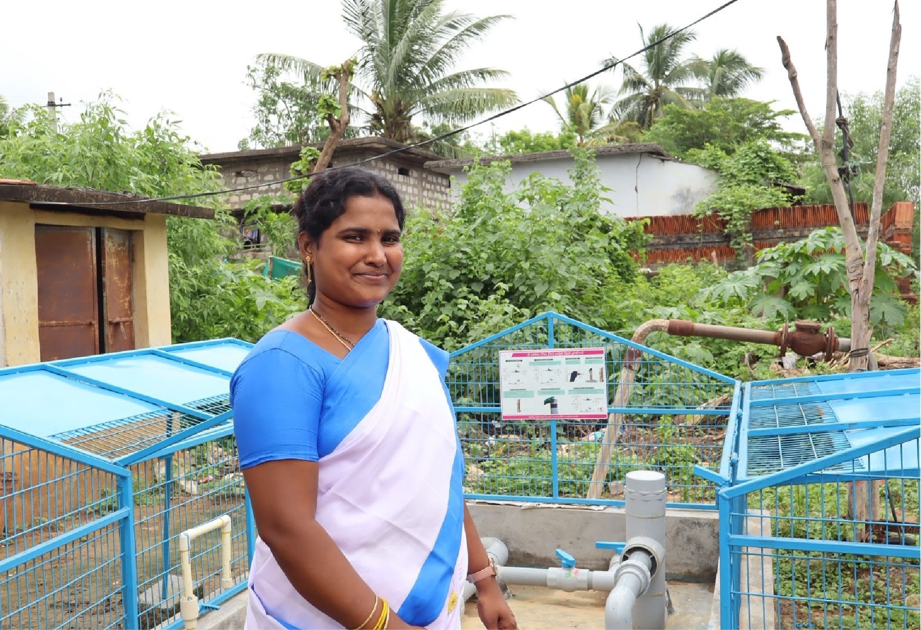 Krishnaveni standing beside an in-line chlorination device installed at a village water source